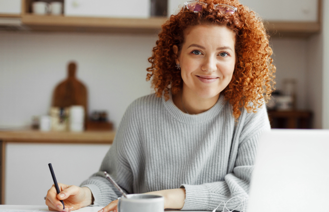 female pr professionals at desk - Search Solution Group red headed pr and communications professional holding pen smiling