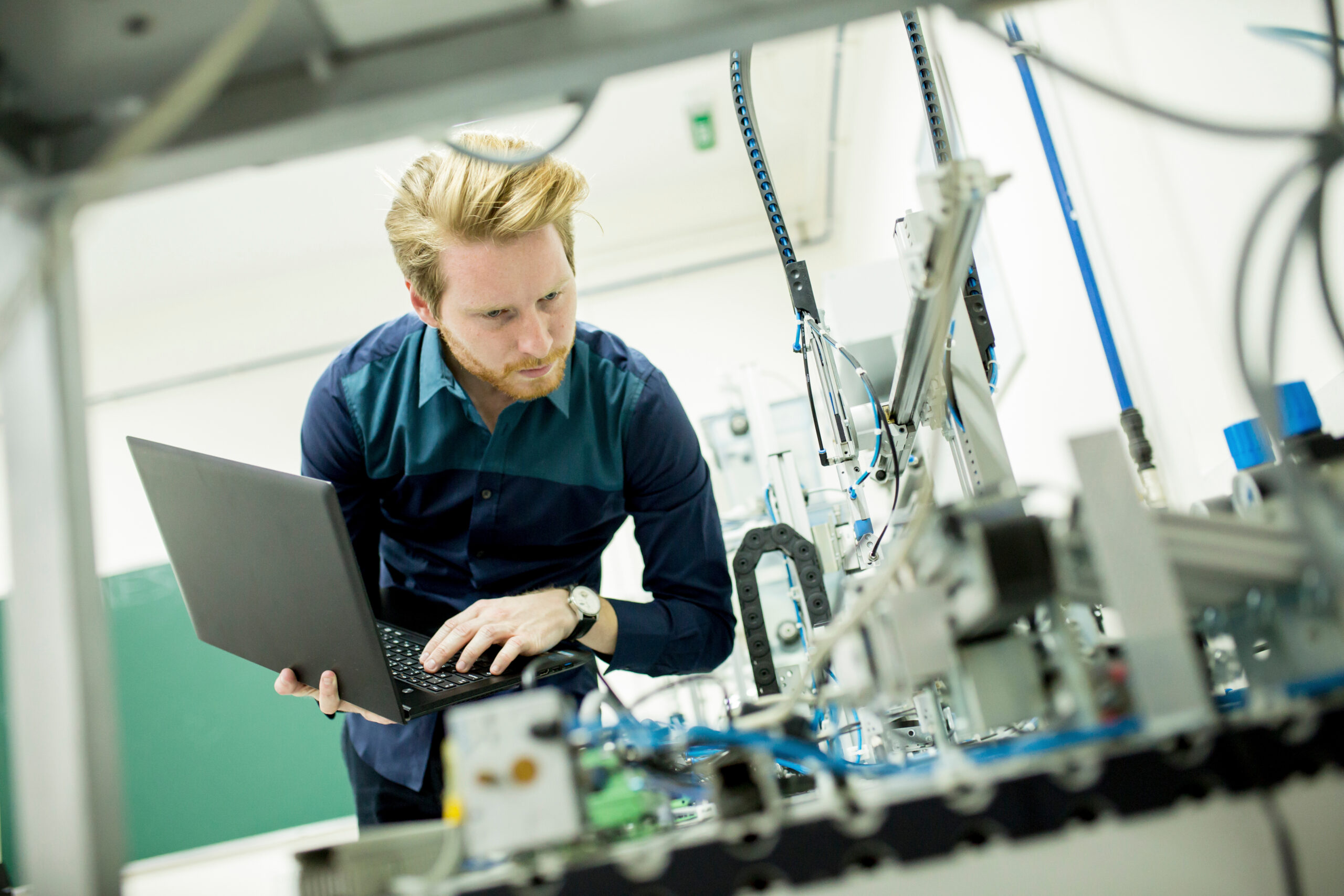 Engineer in the factory - Search Solution Group industrial engineer holding laptop peering over mechanical device