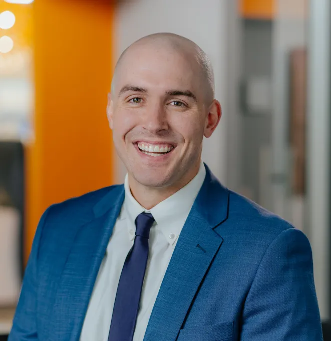 Smiling man in a blue suit and navy tie—professional headshot in an office setting